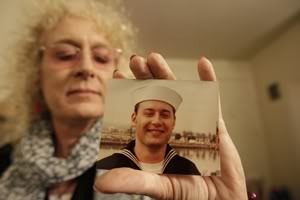 Image: Autumn Sandeen holding photo of herself from when she was in the U.S. Navy. Photo of Autumn in uniform is from 1980. Photo by Gregory Bull.