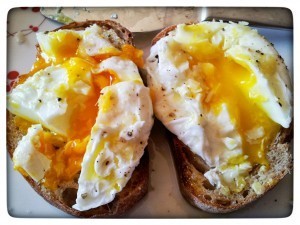 A picture of two poached eggs with the yolks showing. The farm-fresh egg has a a golden-orange yolk, the store-bought egg has a pale yellow yolk.