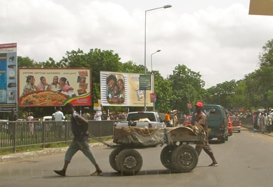 A PAIR OF TRUCK-PUSHERS CROSS THE SOUTHERN END OF BARNES ROAD IN ACCRA
