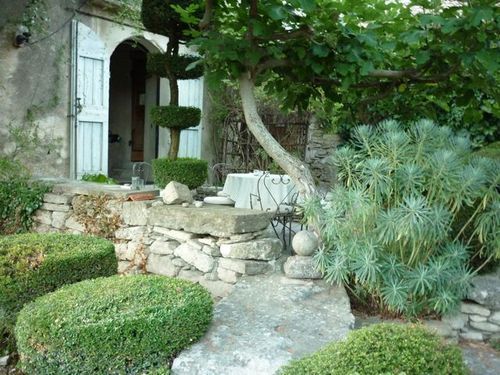stone cottage and window shutters on shaded patio in Provence. Manicured garden with euphorbia and pruned hedges (c) Ann Mah for www.french-word-a-day.com