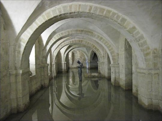 A statue gazes down at its cupped hands. It is reflected in the low surrounding water