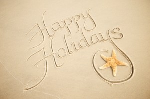 Happy Holidays written in the sand, next to a star fish
