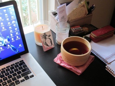 A photo of the desk in my office in Morrow, GA, with computer, candles, desk organizer, notebooks, and a large tea-bowl filled with tea.