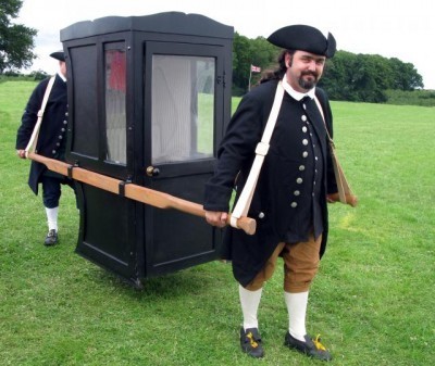 Two costumed men carry a black-painted sedan chair.