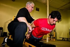 A man in a black shirt helping a man in a red shirt with an exercise