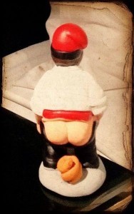 A small Nativity figurine of a man defecating on the ground, from the back.