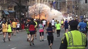 Runners continue to run towards the finish line as an explosion erupts at the finish line of the Boston Marathon