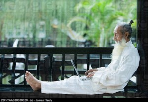 Elderly man in traditional Chinese clothing, barefoot, using laptop