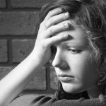 Teenage girl siiting against brick wall in a depressed state