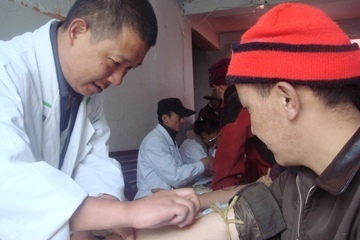 A researcher collects a blood sample from an ethnic Tibetan man participating in a DNA study.