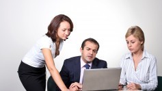 Two people helping a third with something on a laptop