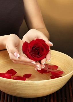 woman hands with wooden bowl of water with petals,