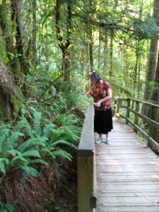 Mollie stands on a bridge, pointing down at a fern-covered ravine
