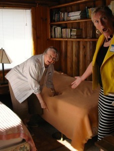 Two women point at a foot sticking out from under a twin bed