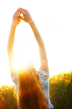 Young woman enjoying sunlight with raised arms