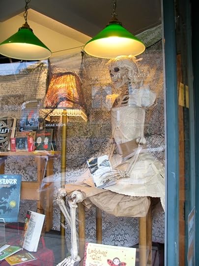 Anni Blooms ' bookstore window features a skeleton clad in a dress of book pages with a book of poetry in her hand