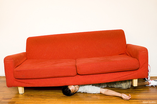 Young man lying under a red couch.
