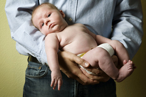 image of man's torso in buttondown and jeans holding an infant