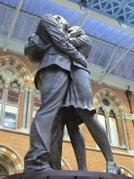 a statue of a man and a woman in modern clothes embracing 
