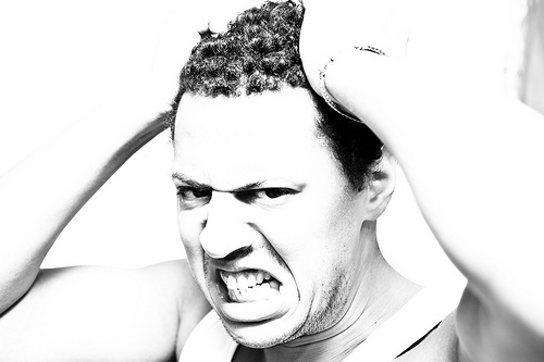 black and white picture of a man grimacing and pulling his hair in frustration 