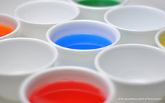 White cups, some empty, some containing multicoloured liquids