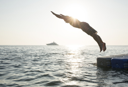 Man dives into tranquil sea, from pier, boat