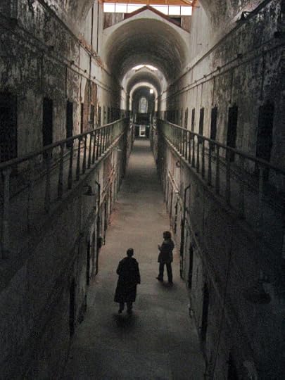 Two men walking through the hallway of an old prison.