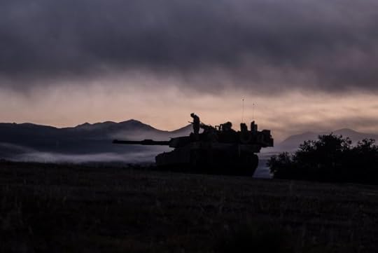 A silhouette of a tank with a man standing on it. It is in front of a sunrise.