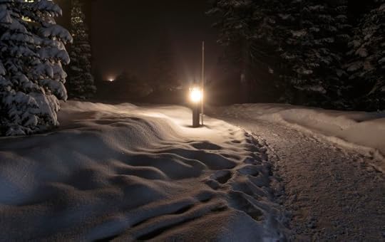 A lit post next to a path, the ground covered in snow.