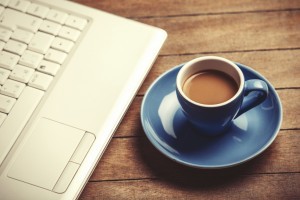 Cup of coffee and laptop on wooden table.