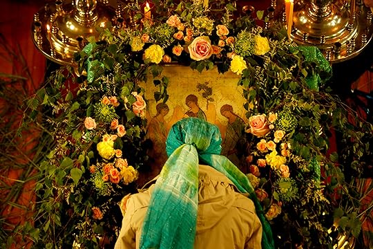 A woman, wearing a green headscarf, venerates the Pentecost icon adorned with greens and flowers.