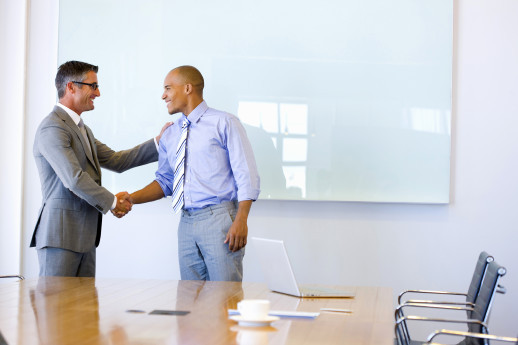 Two executives shaking hands in a meeting room.