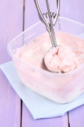 Ice cream in container and ice cream spoon on wooden table close-up