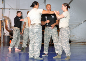 Two women soldiers practicing hand to hand as man watches.