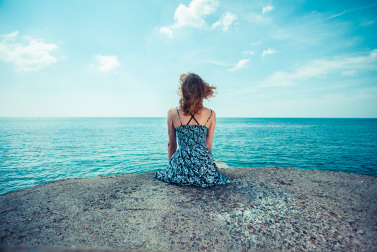 A young woman is sitting on a pier by the ocean