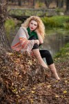 Beautiful woman posing in park during autumn season. Blonde girl wearing green blouse and big shawl posing outdoor. Long fair hair girl with green sweater under a shawl relaxing in autumnal park.