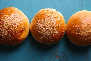 Tasty buns with sesame on color wooden background