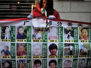 A woman holds a candle behind a board showing photos of missing children during a campaign to spread information to search for them in Wuhan, in central China's Hubei province.