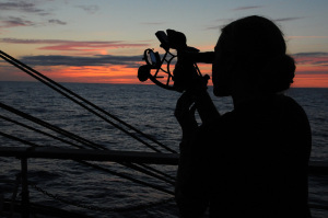 Silhouette of woman officer using a sextant at the rail of ship
