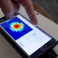 The Walabot sensor board attached to a cellphone looking through drywall to find a hidden pipe.