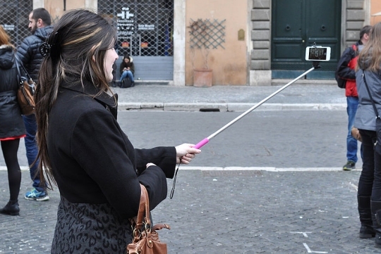 A woman uses a 'selfie stick' to take a selfie. (click for credit)