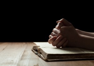 woman hands on bible. she is reading and praying over bible in a dark space over wooden table