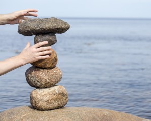 human hand making stack of large round stones near the water, which are due to the balance