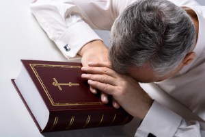 Photo of sad old man praying to God with Bible