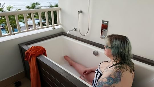 Me, in a black and white striped swimsuit, sitting in a bathtub on the balcony, staring blankly out at the ocean. There is no water in the bathtub.
