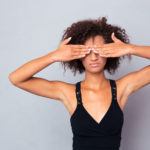 Portrait of afro american woman covering her eyes over gray background
