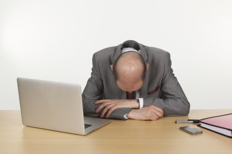 Despairing businessman with his head down resting on his arms on his desk as he contemplates the hopelessness of his position