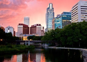 Publicity photo showing the tall buildings of downtown Omaha over a lake at dusk.