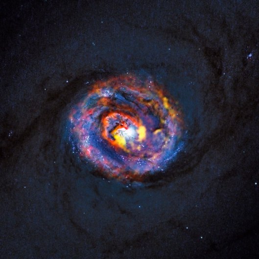 This detailed view shows the central parts of the nearby active galaxy NGC 1433. The dim blue background image, showing the central dust lanes of this galaxy, comes from the NASA/ESA Hubble Space Telescope. The coloured structures near the centre are from recent ALMA observations that have revealed a spiral shape, as well as an unexpected outflow, for the first time.