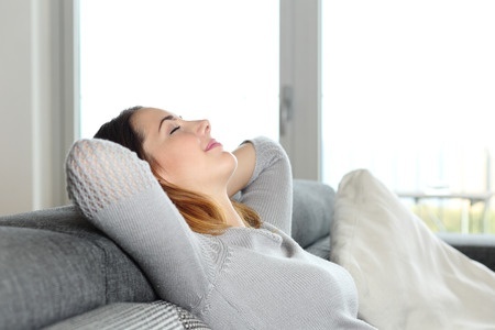 31105719 - happy relaxed woman resting on a couch at home with arms in the head